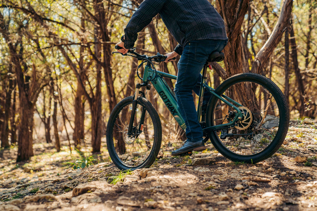A man riding the GOTRAX D1RT Electric Mountain Bike on an off-road trail.