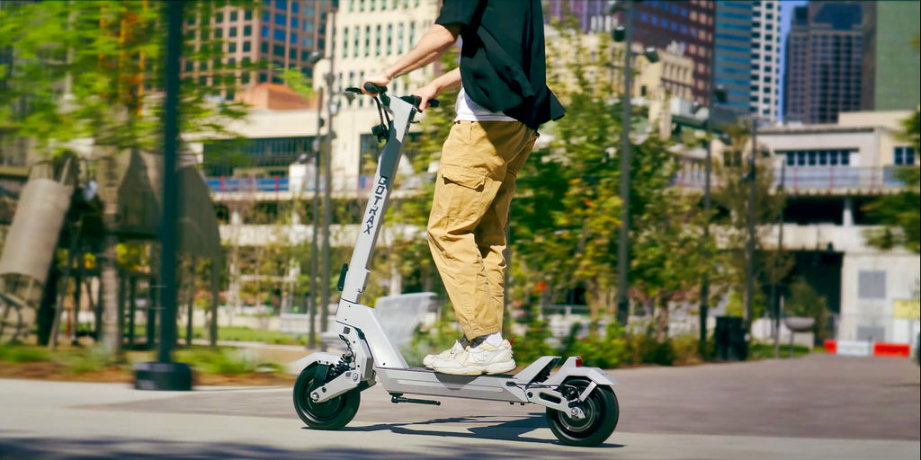 A man riding the GOTRAX GX2 Dual Motor Electric Scooter down a city street.