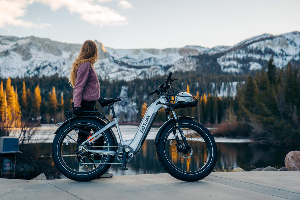 A woman standing by a lake with the GOTRAX Tundra Fat Tire Electric Bike